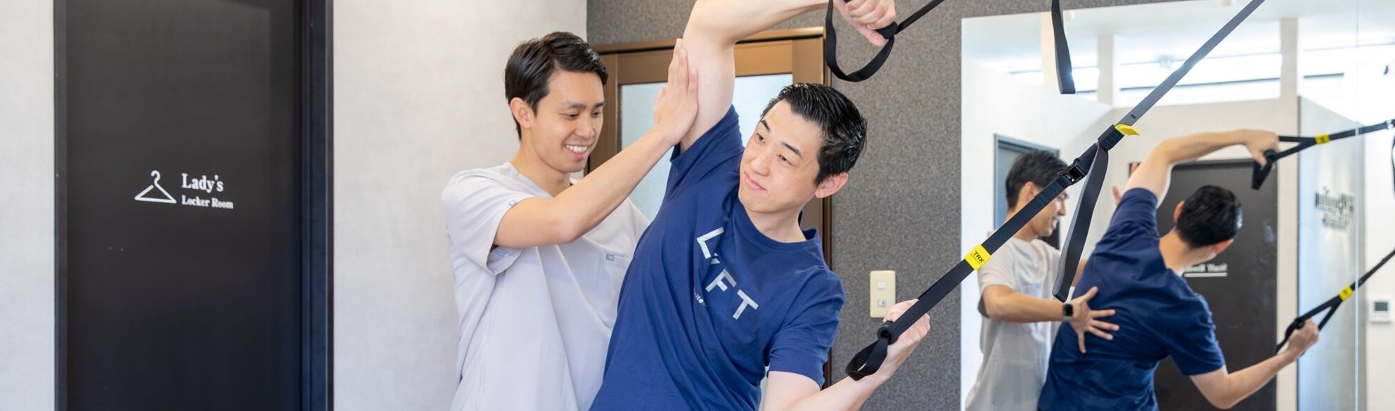 器具を使ってトレーニングを行う男性とサポートするトレーナー