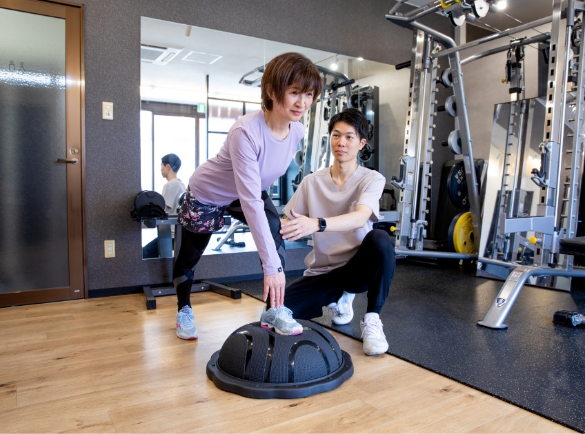 トレーナーが姿勢を確認しながら、片脚でバランストレーニングを行う女性