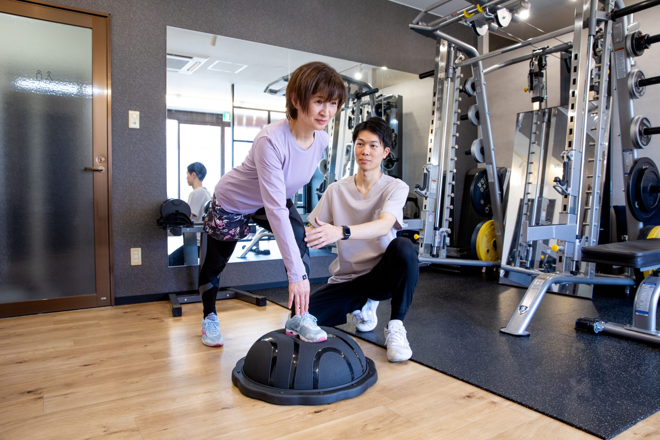 トレーナーが姿勢を確認しながら、片脚でバランストレーニングを行う女性