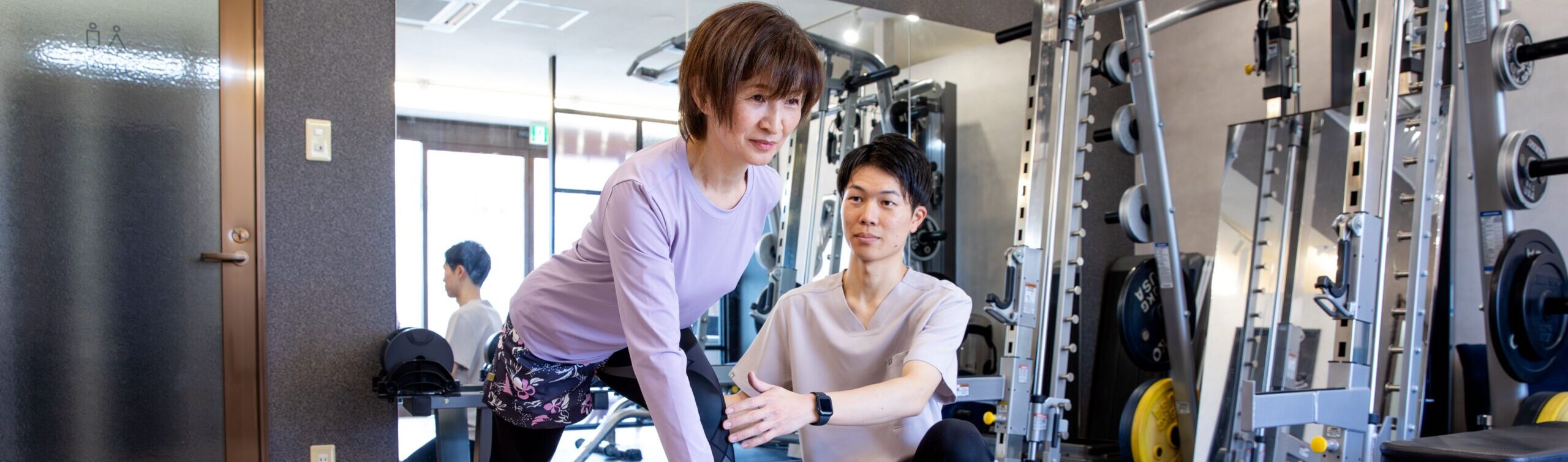 トレーナーが姿勢を確認しながら、片脚でバランストレーニングを行う女性