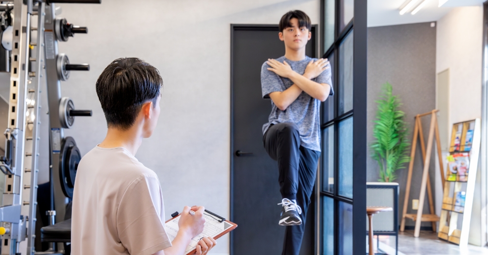 胸の前で手をクロスして足上げを行う子どもと見守るトレーナー