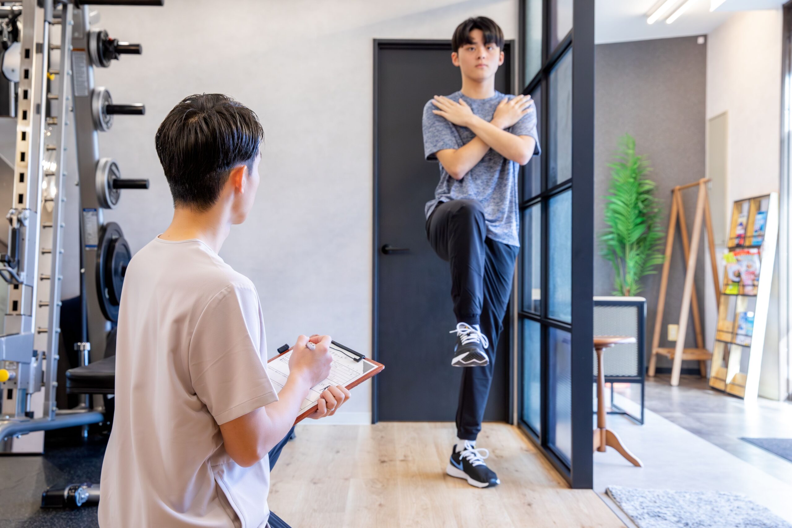 胸の前で手をクロスして足上げを行う子どもと見守るトレーナー