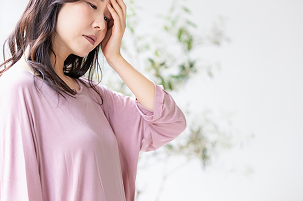 めまいを覚えて手で頭を支える女性